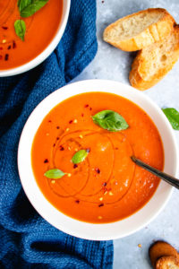 Roasted tomato soup served with bread and topped with basil and chili flakes.