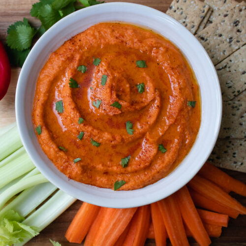 The Hummus in a bowl topped with fresh cilantro and with vegetables and crackers on the side.