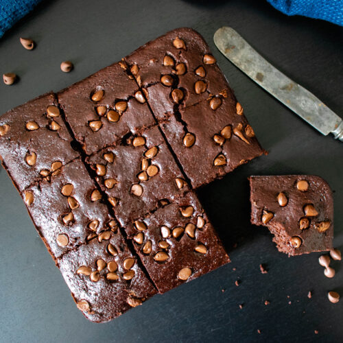 The brownies cut in pieces with a knife on the side.