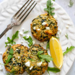 Baked Greek Zucchini and Quinoa Fritters served on a plate with some feta cheese and a slice of lemon.