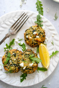 Baked Greek Zucchini and Quinoa Fritters served on a plate with some feta cheese and a slice of lemon.