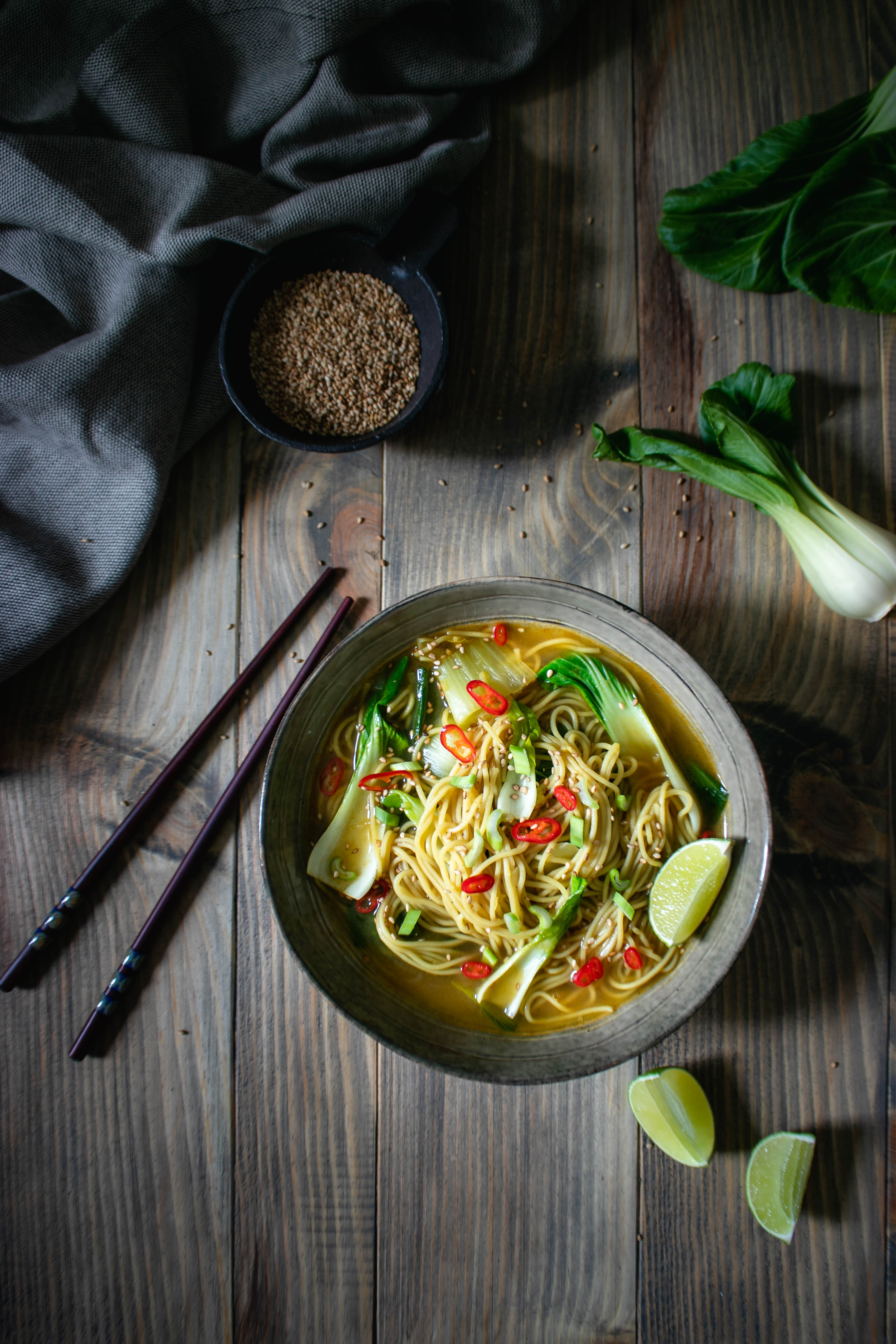 Warming Vegan Noodle Soup with red curry and Bok Choy served in a bowl topped with chili, lime and sesame seeds 