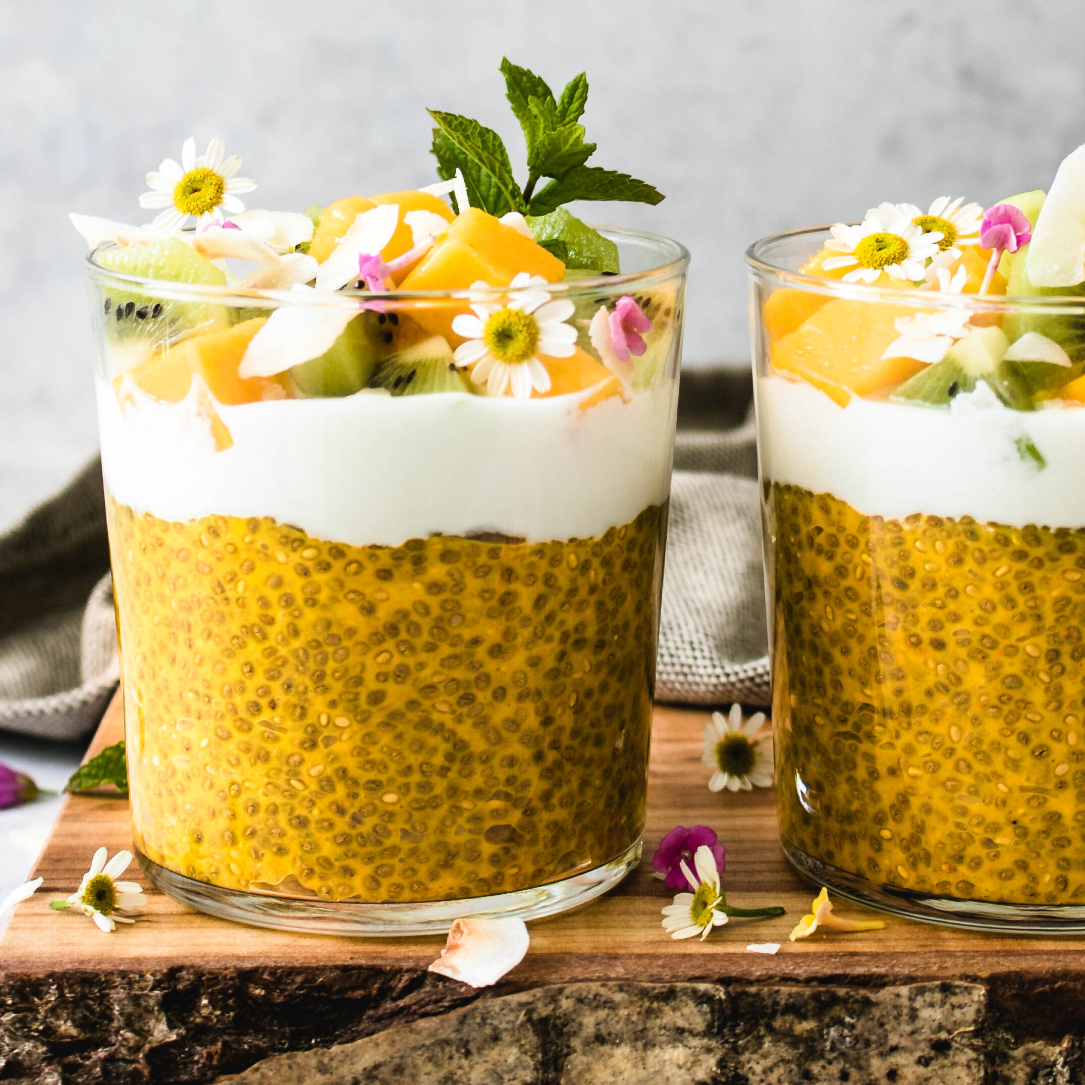 Mango Chia Pudding in two glasses topped with fresh fruit and coconut.