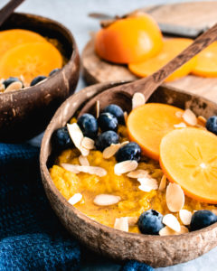 Persimmon Oatmeal served in a bowl topped with fresh persimmons, blueberries and almonds.