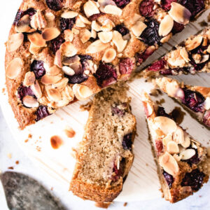 Vegan cherry cake topped with cherries and sliced almonds, cut into slices on a board.