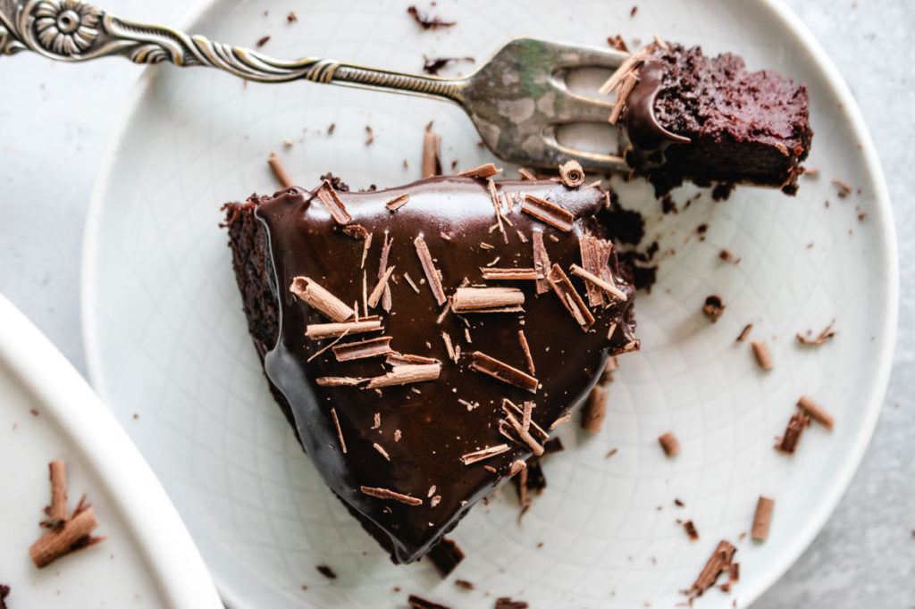 A slice of Vegan Beetroot Chocolate Cake served on a plate with a pice cut off with a fork.
