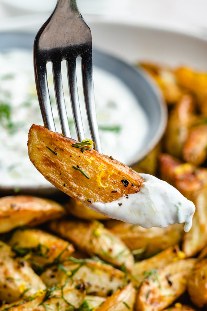 Roasted Greek Potato on a fork being dipped in the lemon tzatziki sauce. 