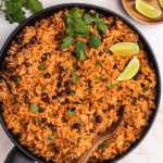 Vegan Mexican rice and black beans in a pan garnished with cilantro and lime