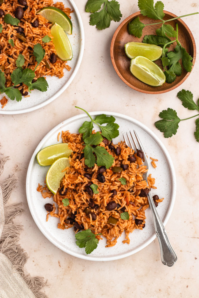 Vegan Mexican rice and black beans plated on two plates with fresh cilantro and lime wedges 