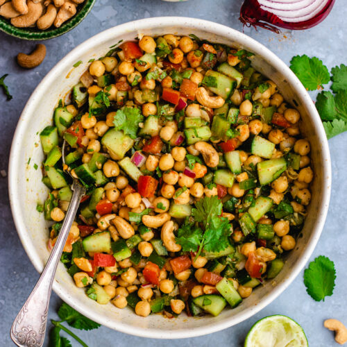 Indian chickpea salad served in a salad bowl with some cashew nuts and lime.