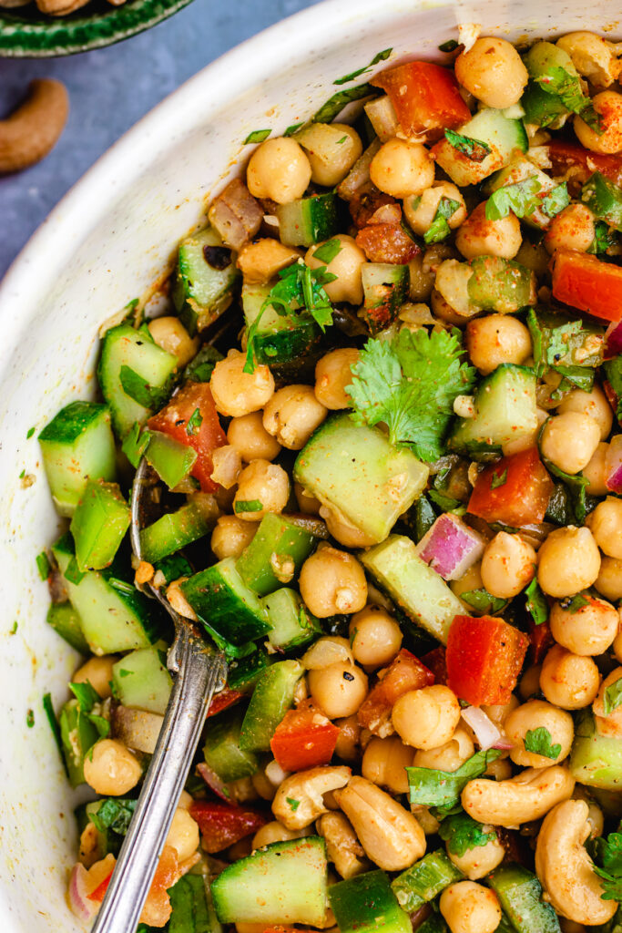 Close up of this Indian chickpea salad served in a white bowl with a bid spoon.