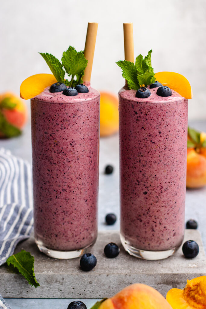 Peach Blueberry Smoothie served in 2 tall glasses topped with mint, blueberries and a slice of peach.