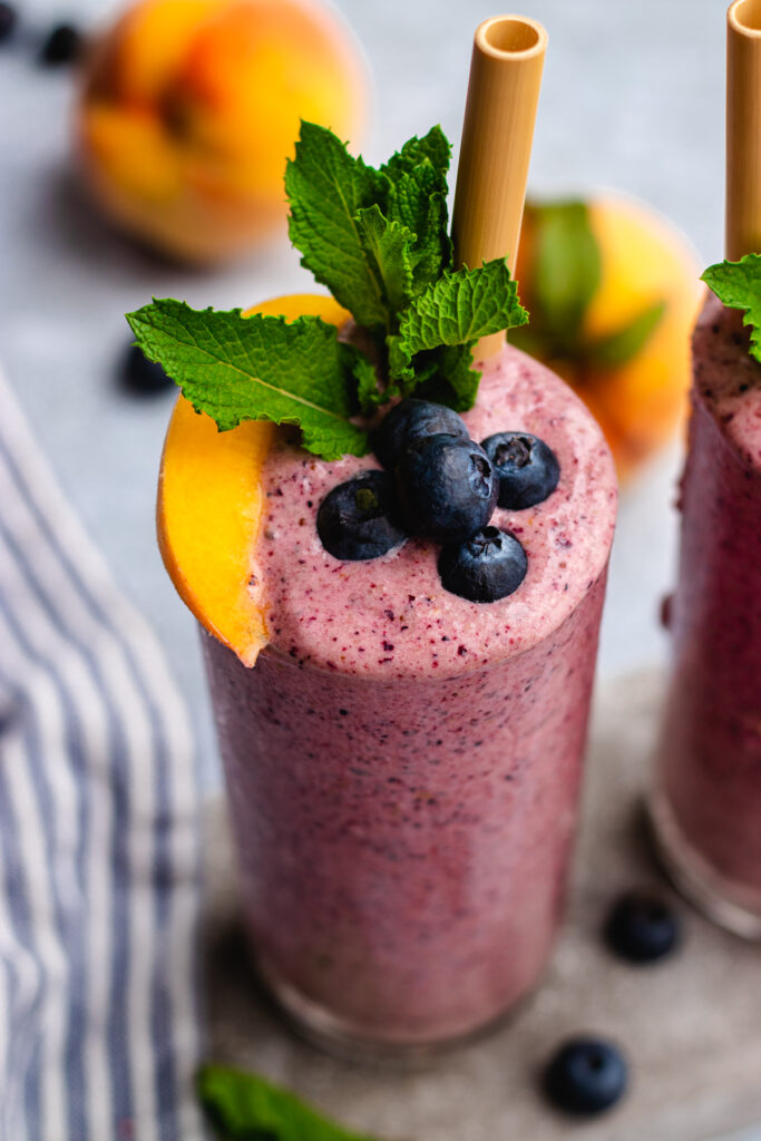 Peach Blueberry Smoothie served in 2 tall glasses topped with mint, blueberries and a slice of peach.
