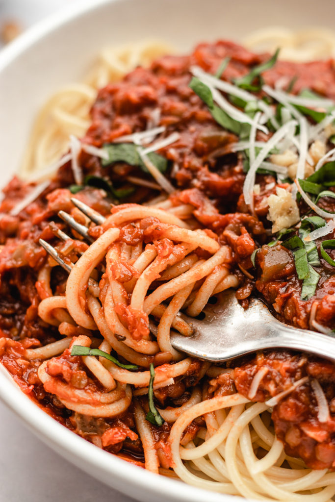 Closeup of a bowl of spaghetti and walnut lentil bolognese topped with parmesan and basil. The spaghetti is twirled  around the fork.
