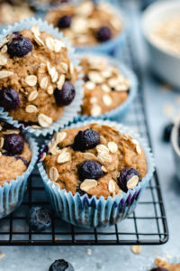 Banana blueberry oatmeal muffins stacked together on a cooling rack topped with oats and blueberries.