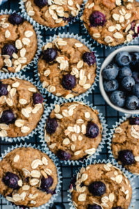 Banana blueberry oatmeal muffins stacked together on a cooling rack topped with oats and blueberries.