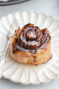 air fryer cinnamon roll topped with frosting served on a small plate.