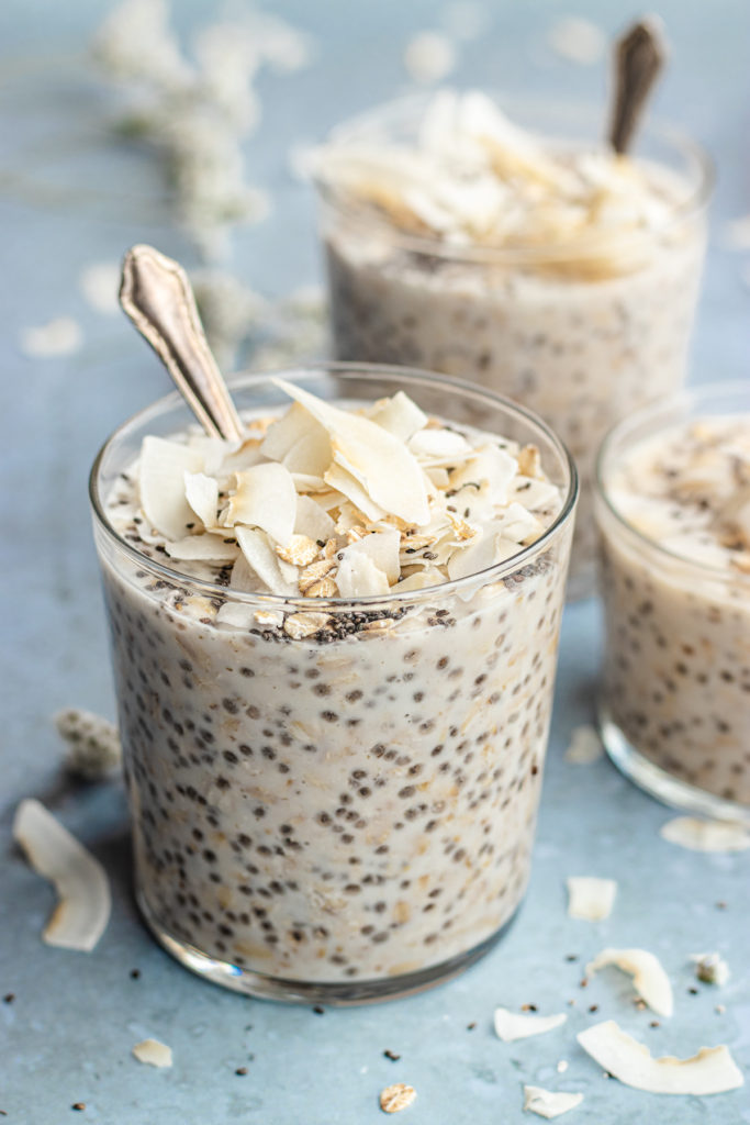 coconut milk overnight oats served in glasses topped with coconut chips, chia seeds and oats.