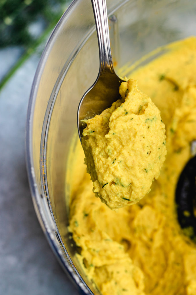 A spoon full of creamy lemon dill hummus being taken out of the food processor.