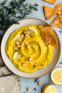 Lemon dill hummus served in a bowl with pita chips.