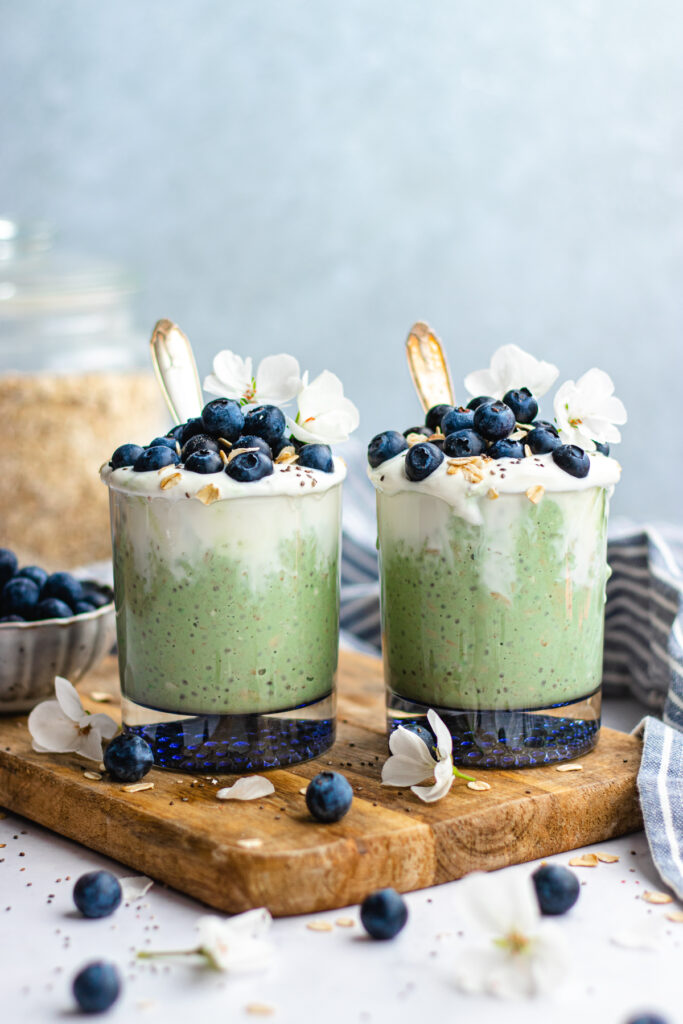 Matcha overnight oats served in two glasses toped with yoghurt, blueberries and some oats.