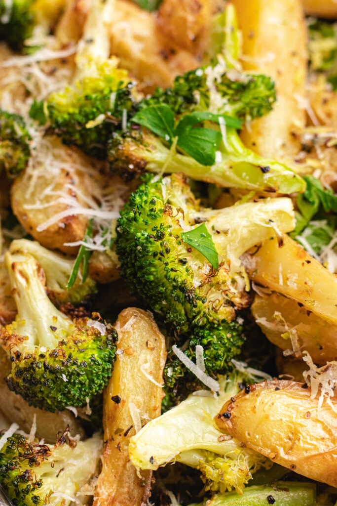 Roasted potatoes and broccoli on a baking tray topped with parmesan and chopped parsley.