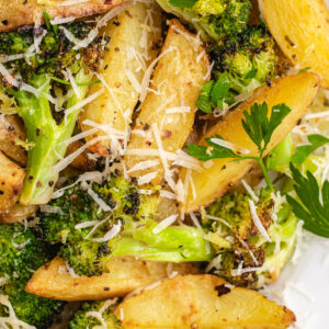 Roasted potatoes and broccoli on a serving plate topped with parmesan and chopped parsley.