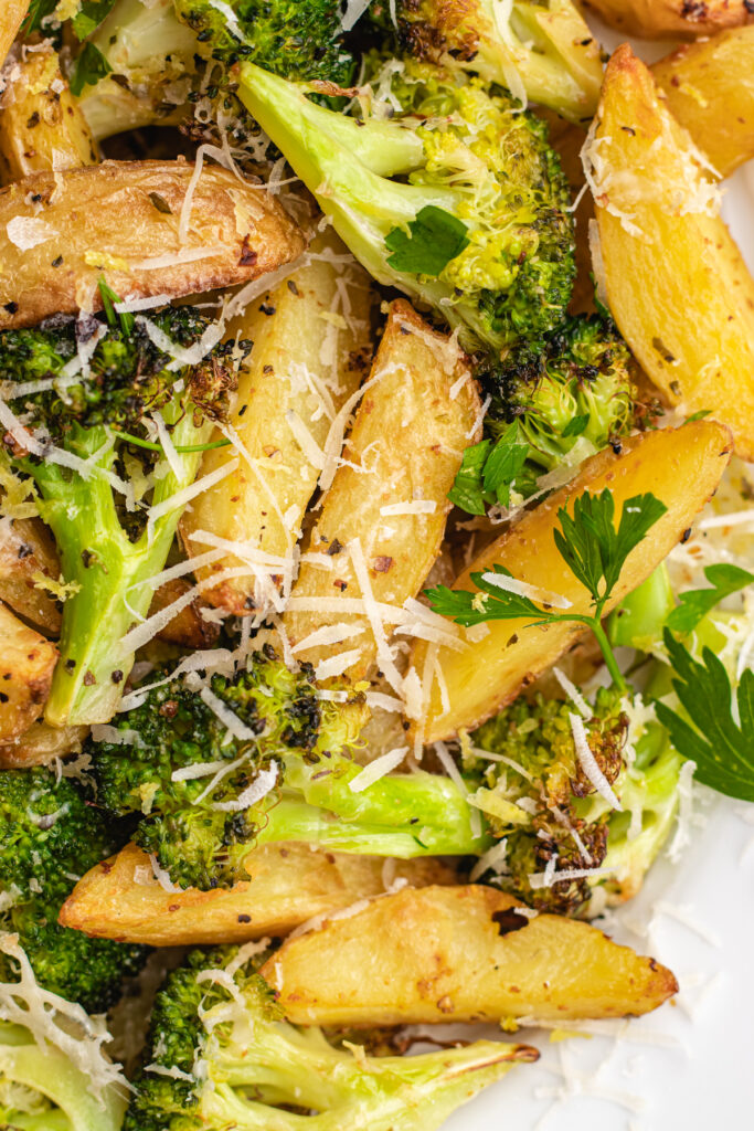 Roasted potatoes and broccoli on a baking tray topped with parmesan and chopped parsley.