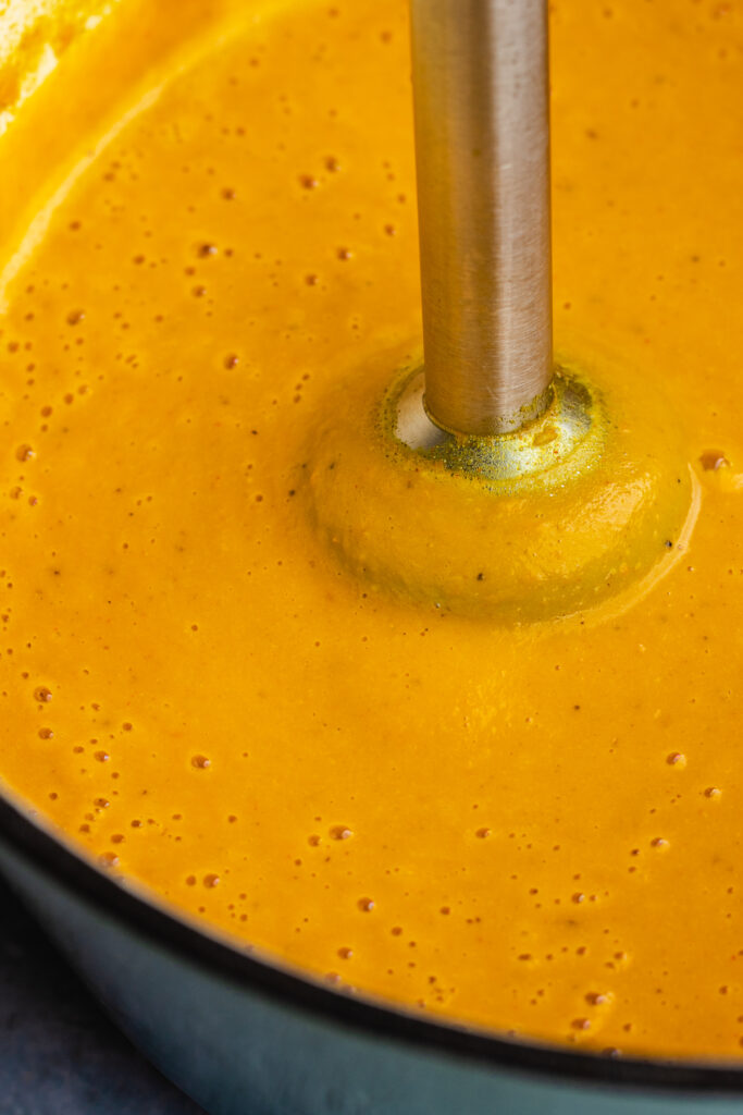 The soup being blended to smooth with a hand held blender in the pot.