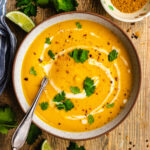 Spiced carrot and lentil soup served in a bowl topped with a swirl of coconut milk, cilantro and chili flakes.