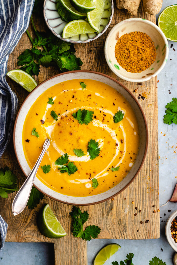 Spiced carrot and lentil soup served in a bowl topped with a swirl of coconut milk, cilantro and chili flakes.
