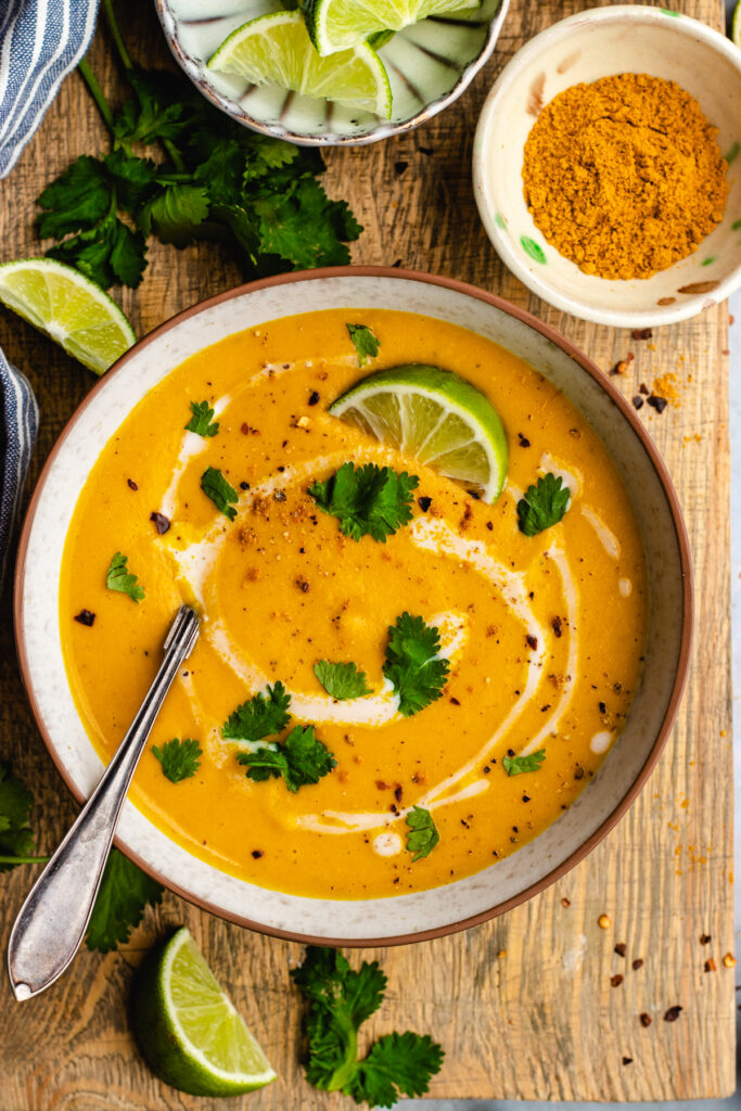 Spiced carrot and lentil soup served in a bowl topped with a swirl of coconut milk, cilantro and chili flakes.