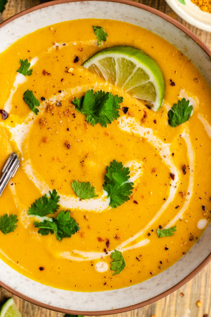 Spiced carrot and lentil soup served in a bowl topped with a swirl of coconut milk, cilantro and chili flakes.