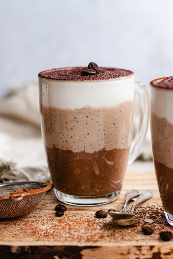 Tiramisu Overnight Oats served in 2 glass coffee cups topped with cocoa powder and coffee beens.