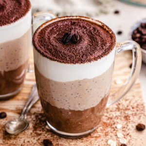 Tiramisu Overnight Oats served in 2 glass coffee cups topped with cocoa powder and coffee beens.