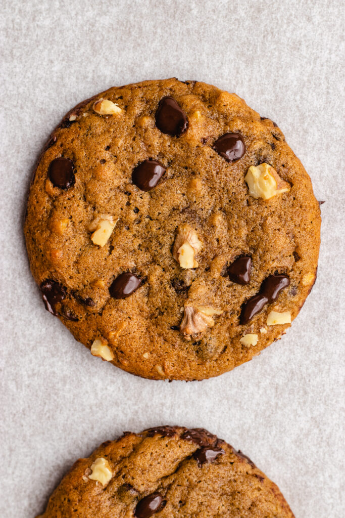 Close-up of a cookie topped with chocolate chips and walnuts. 