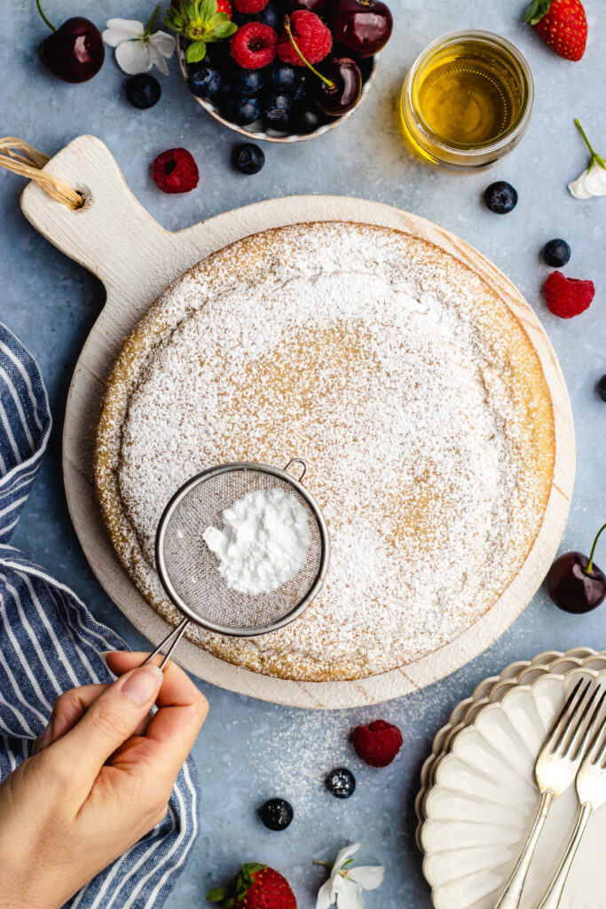 Dusting the baked vegan olive oil cake with powdered sugar.