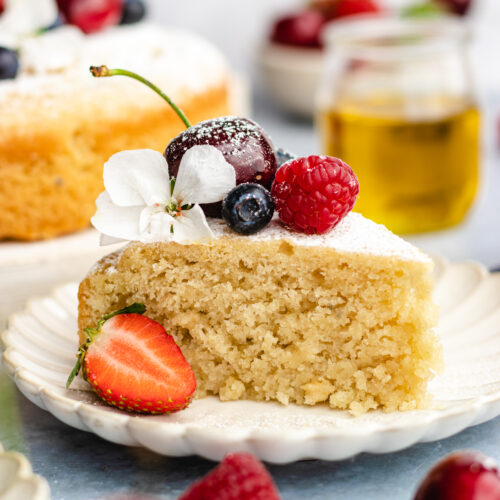 A slice of Vegan olive oil cake topped with fresh berries and flowers.