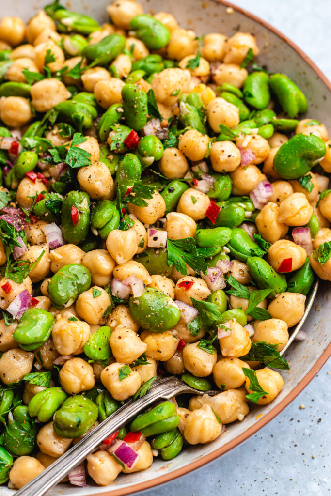 Fava bean chickpea salad served in a bowl with a serving spoon.