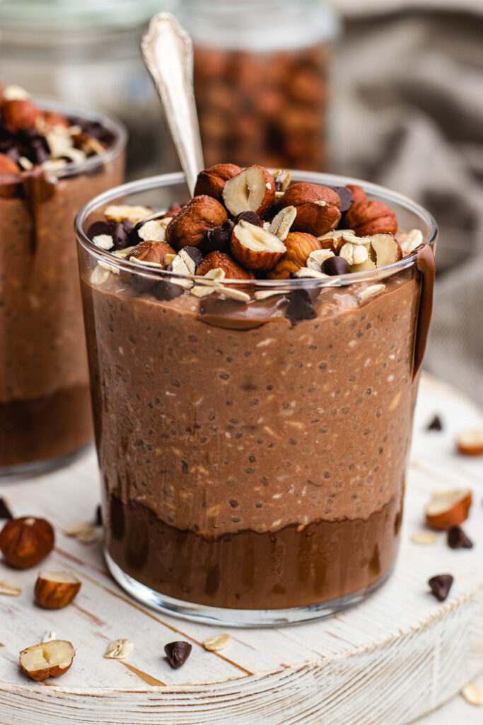 Nutella overnight oats served in a glass. Topped with hazel nuts, chocolate chips and Nutella.