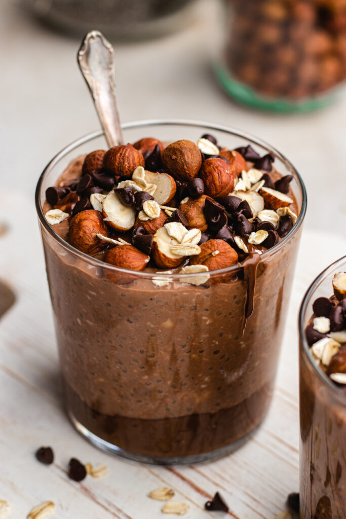 Nutella overnight oats served in a glass. Topped with hazel nuts, chocolate chips and Nutella.