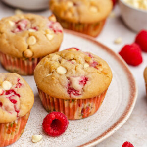 Raspberry White Chocolate Muffins served on a plate with some fresh raspberries and white chocolate chips.