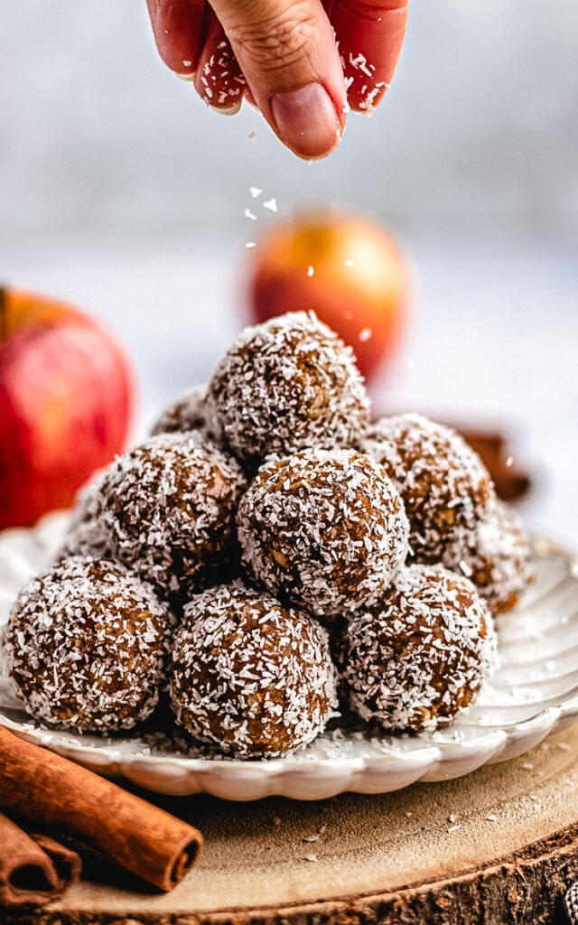 Apple Pie Bliss Balls on a small plate being topped with coconut.