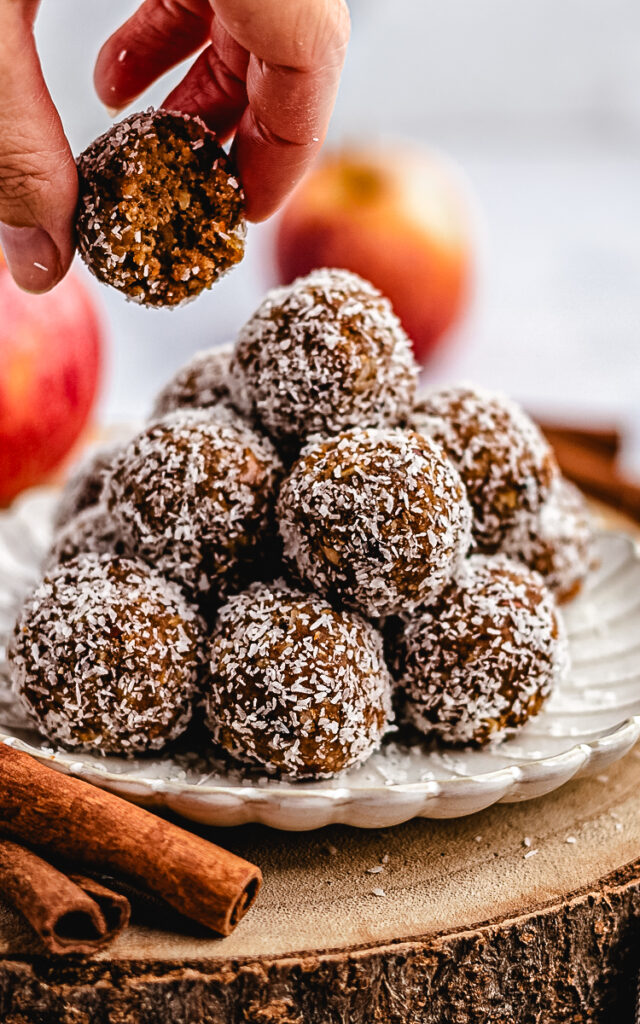 A stack of Apple Pie Bliss Balls on a small plate with one cut in half lifted by a hand.