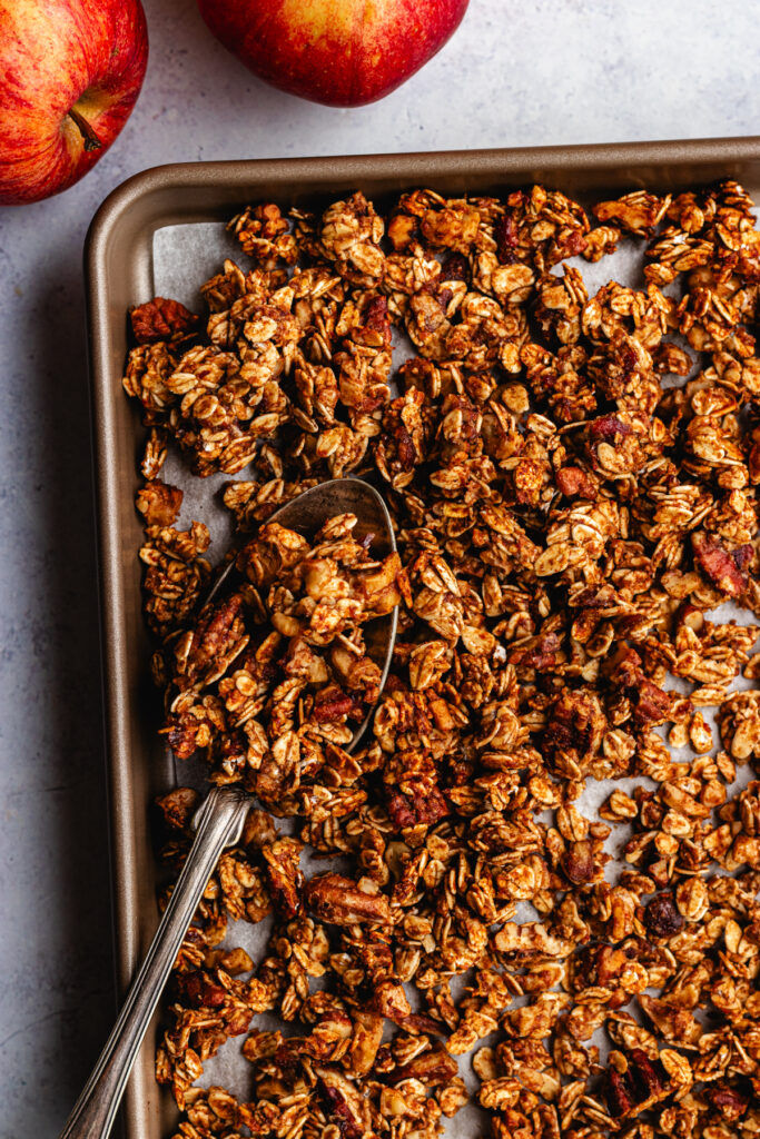 Apple Pie Granola on a baking tray with a spoon.