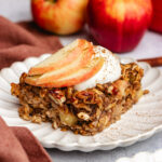 A pice of Apple pie baked oats on a plate topped with yoghurt and apple slices.