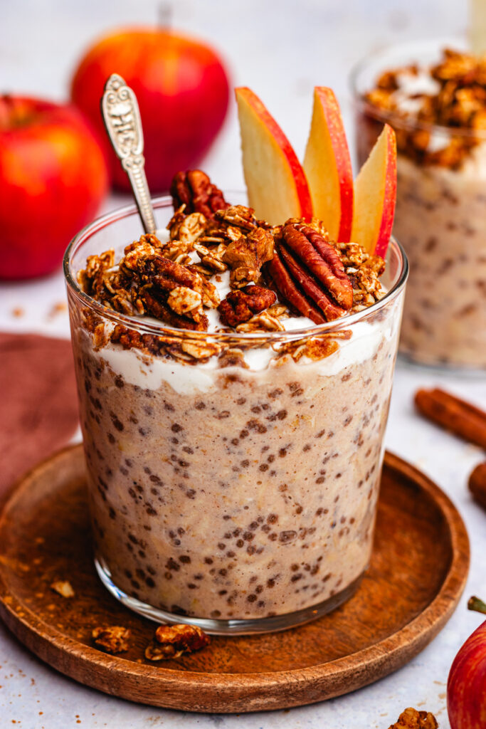 Applesauce overnight oats in a glass topped with yoghurt, granola and fresh apple slices.