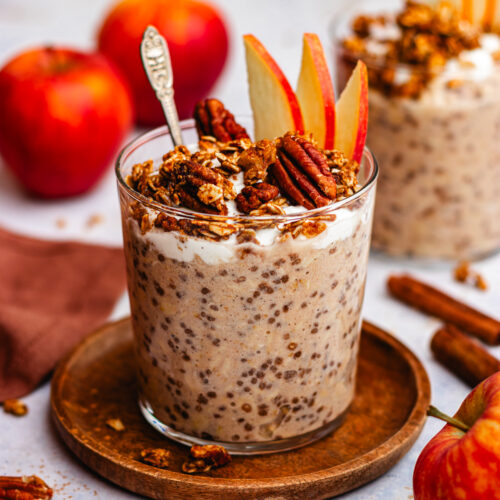 Applesauce overnight oats in a glass topped with yoghurt, granola and fresh apple slices.