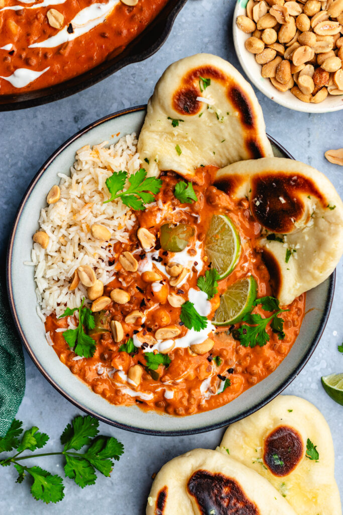 Chickpea and lentil curry served in a bowl with naan bread. Topped with yoghurt, cilantro and peanuts. 