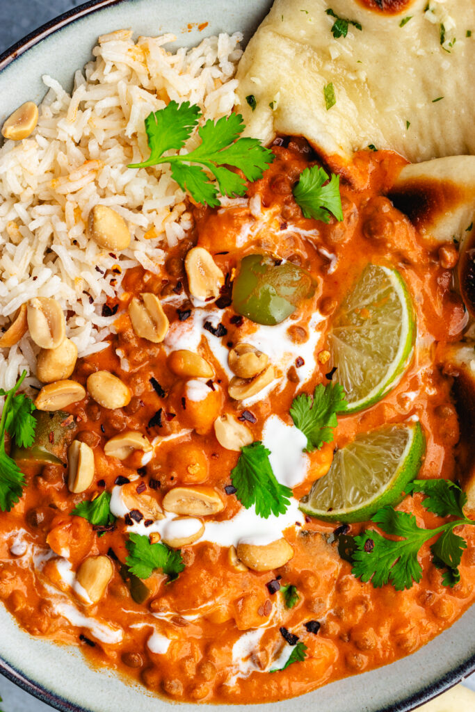 Chickpea and lentil curry served in a bowl with naan bread. Topped with yoghurt, lime slices, cilantro and peanuts.